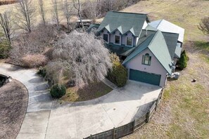 A two-story house with a green roof, a driveway, and a fenced yard. - Creek-side home with private hot tub, game room, firepit, deck & mountain view (Whittier)