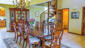 A dining area with a large wooden table, ornate chairs, a chandelier, and a staircase leading to an upper level. - Meadow Creek Manor (Whittier)