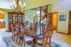 A dining room with a large wooden table and chairs, a chandelier, and a staircase leading to another level. - Creek-side home with private hot tub, game room, firepit, deck & mountain view (Whittier)