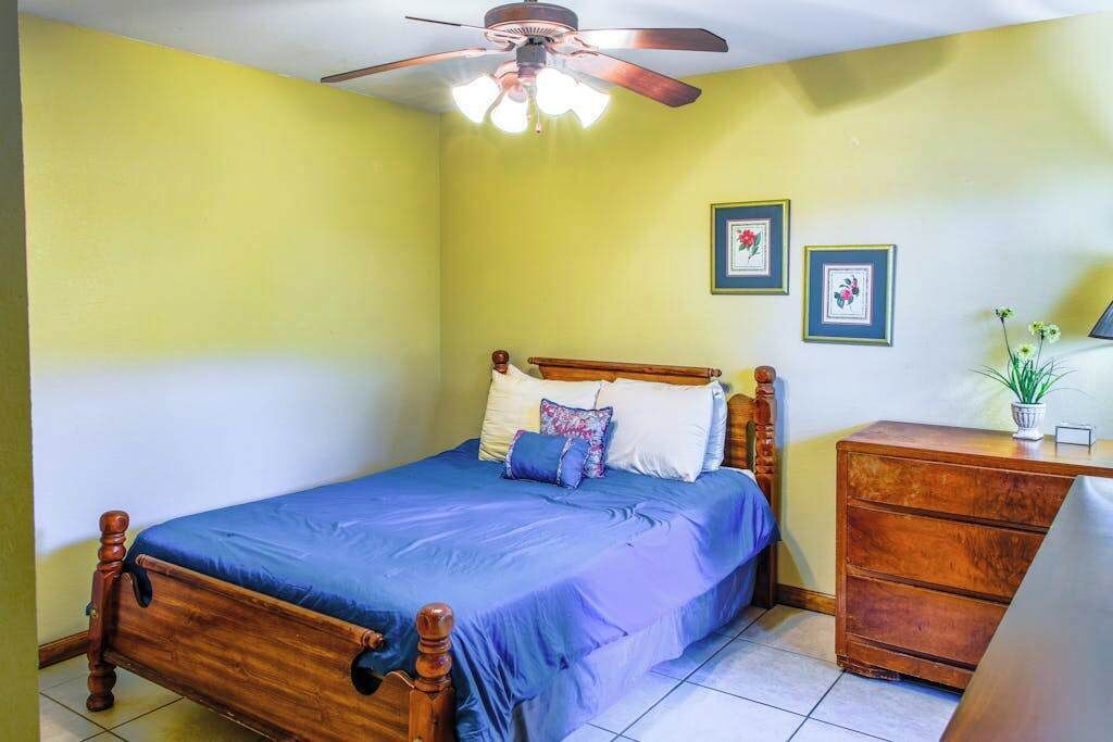 A bedroom with a bed, wooden headboard, ceiling fan, and a dresser.