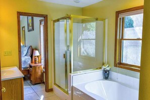 A bathroom with a glass-enclosed shower, a bathtub, a sink, and a window. - Creek-side home with private hot tub, game room, firepit, deck & mountain view (Whittier)