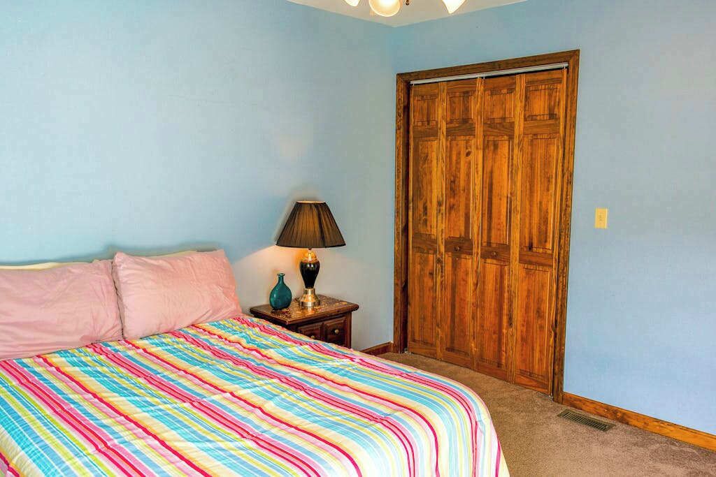 A bedroom with a bed, a nightstand with a lamp, and a wooden wardrobe.
