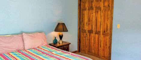 A bedroom with a bed, a nightstand with a lamp, and a wooden wardrobe.