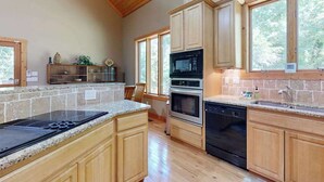 Una cocina con armarios de madera, encimera de granito, estufa integrada, microondas, horno y lavavajillas.