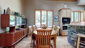 Un comedor con mesa y sillas de madera, un armario de madera con puertas de vidrio y una cocina con detalles de piedra.