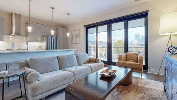 A modern living room with a sofa, coffee table, and a view of the city through large windows. - Modern art-deco condo with balcony, central AC, & washer/dryer - dogs OK (Asheville)