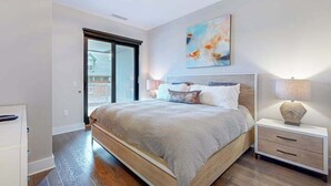 A bedroom with a bed, a nightstand, a lamp, a painting, and a sliding glass door. - Modern art-deco condo with balcony, central AC, & washer/dryer - dogs OK (Asheville)