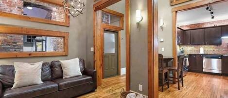 A spacious living area with a leather sofa, wooden flooring, and a kitchen with modern appliances.