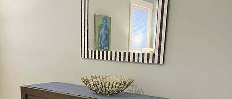 Un aparador de madera oscura con varios cajones y un cuenco decorativo encima, frente a una pared clara con un espejo a rayas en la parte superior.
