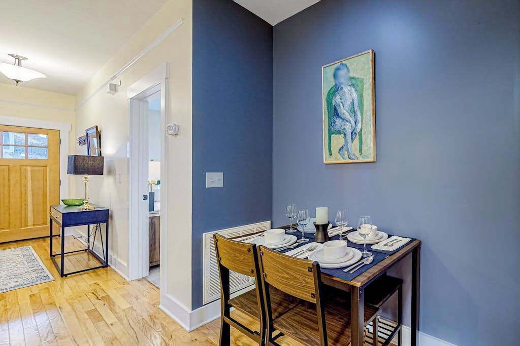 A dining area with a table set for four, a painting on the wall, and a hallway leading to another room.