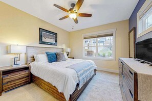 Ein Schlafzimmer mit Bett, Nachttischen, Deckenventilator, Fernseher und Fenster.