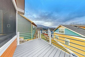 Eine Holzterrasse mit Metallgeländer, die einen Blick auf bunte Häuser und einen Berg im Hintergrund freigibt.