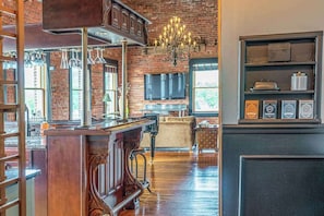 A spacious room with a brick wall, a wooden bar, a chandelier, and a television mounted on the wall.