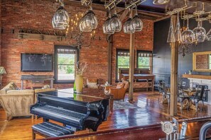 A spacious living room with a grand piano, a brick wall, and a chandelier.