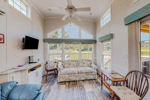 A spacious room with a ceiling fan, a sofa, a wooden table, and a TV.