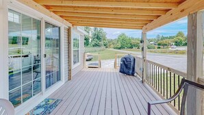 A covered porch with a wooden ceiling, glass sliding doors, a barbecue grill, and a view of a green landscape. - Pet Friendly Tiny home in Great Location with Grill and Covered Porch (Hendersonville)