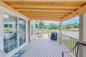 A covered porch with a wooden ceiling, glass sliding doors, a barbecue grill, and a view of a green landscape.