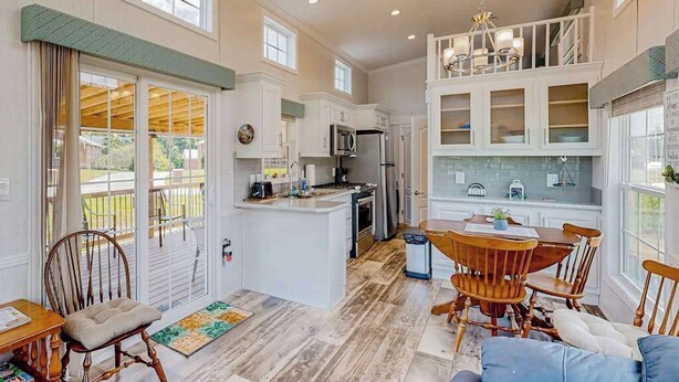A spacious kitchen with a dining area, large windows, and a view of the outdoors. - Pet Friendly Tiny home in Great Location with Grill and Covered Porch (Hendersonville)