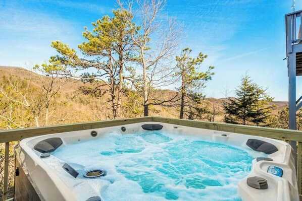 Ein Whirlpool mit einer Holzterrasse, umgeben von Bäumen und Hügeln.