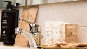 Une salle de bain avec un robinet moderne, une bouteille de shampoing noire et plusieurs trousses de toilette.