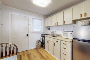 A compact kitchen with white cabinets, a stainless steel refrigerator, a microwave, and a sink.