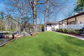 A building with a covered porch, a grassy lawn, and a body of water.