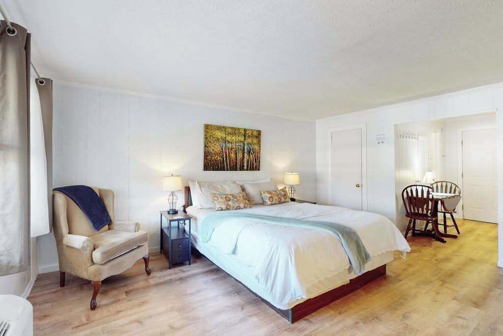 Un dormitorio con cama, mesitas de noche, una silla y un cuadro en la pared.