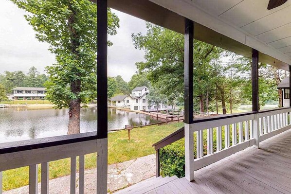 A covered porch with a view of a lake, a bridge, and houses in the background.