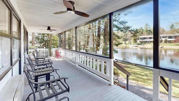 A covered outdoor area with a row of benches, a white railing, and a view of a lake. - Dog-friendly lakefront condo with pool, canoes, & WiFi - in a perfect location (Flat Rock)