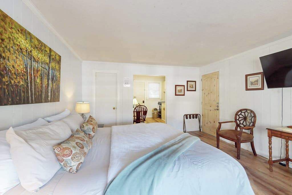 Un dormitorio con cama, escritorio, silla, televisor y un cuadro en la pared.