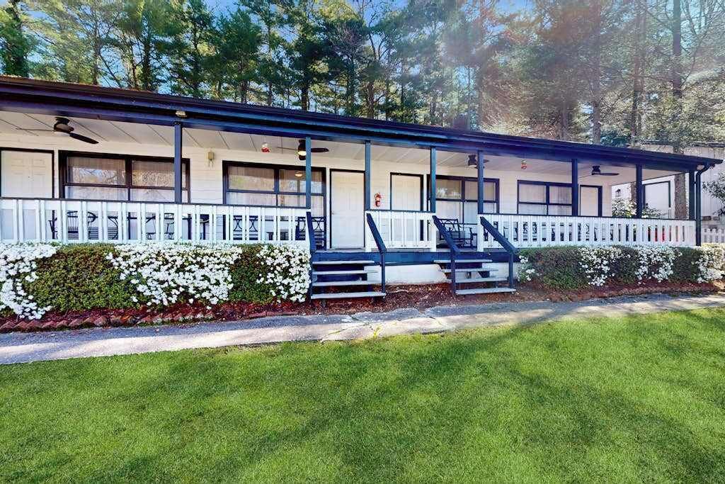 Un motel con porche cubierto, varias habitaciones y un césped cuidado.