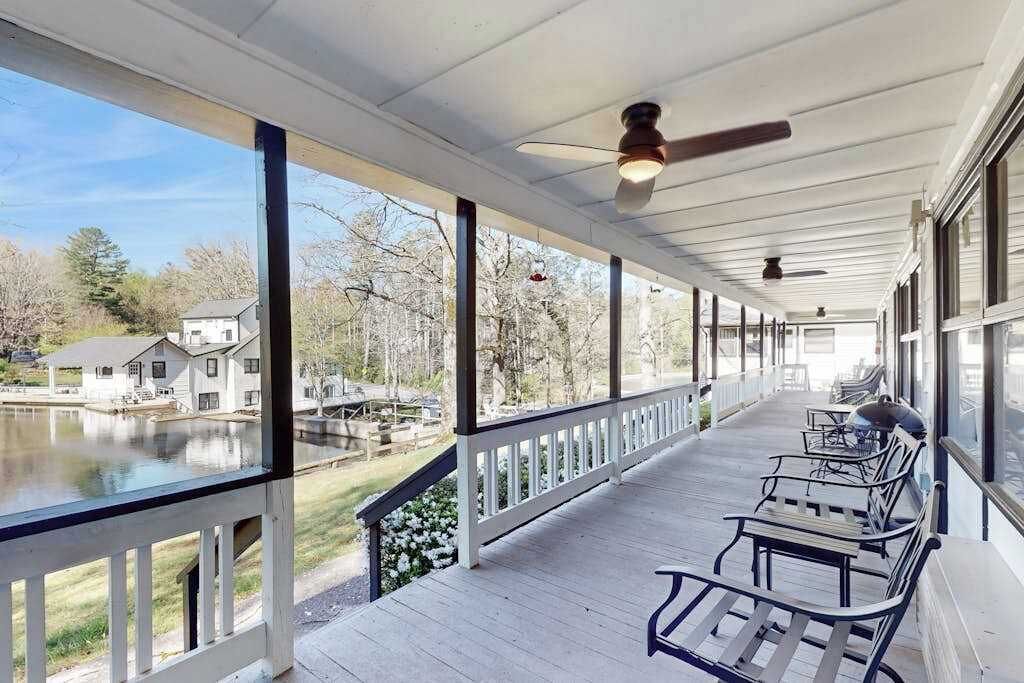 A covered porch with a view of a lake, wooden benches, and ceiling fans.