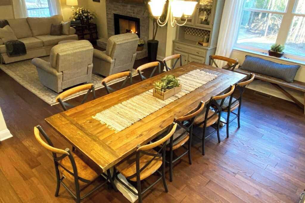 A dining area with a wooden table, six chairs, a rug, and a fireplace in the background.