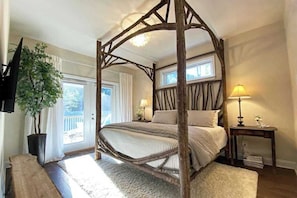 Ein Bett mit Baldachin und Holzrahmen, ein an der Wand befestigter Fernseher, ein Blumentopf und ein Fenster mit Vorhängen.