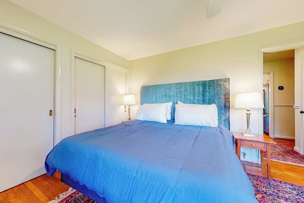 A bedroom with a bed, two bedside tables with lamps, a door, and a patterned rug.