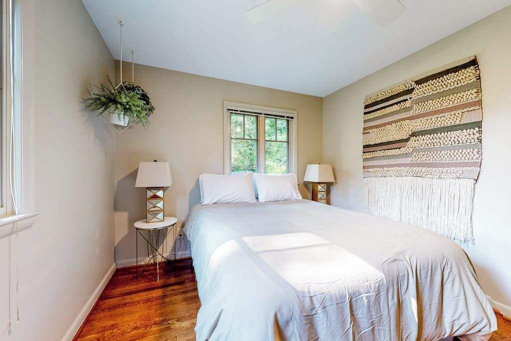 A bedroom with a bed, two bedside tables, a hanging plant, a window, and a wall tapestry.