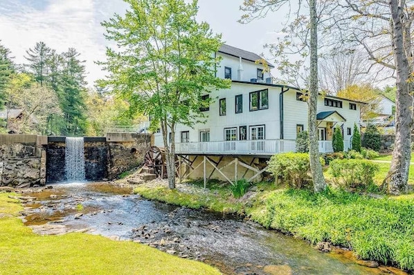 A two-story house with a waterfall, a wooden deck, and a stone bridge.