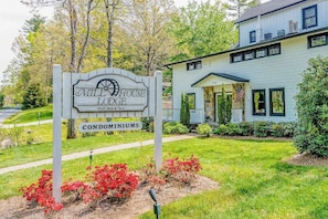 A sign for Mill House Lodge Condominiums with a house in the background.