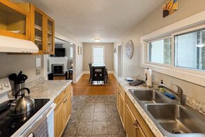 A modern kitchen with granite countertops, stainless steel appliances, wooden cabinets, a dining area with a table and chairs, and a large window providing natural light. - Well-appointed home with a gas grill and fire table (Candler)