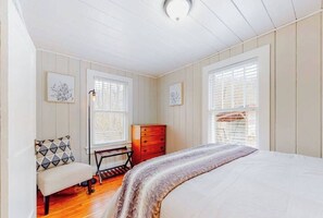 A bedroom with a bed, a dresser, a bench, and two windows with blinds. - Well-appointed home with a gas grill and fire table (Candler)