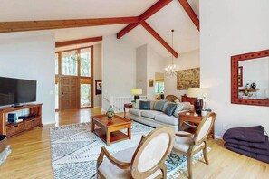 A spacious living room with a large TV, wooden furniture, and a staircase leading to another level. - Idyllic Mountain Escape | Grill, Outdoor Lounge | 4 Mins to Flat Rock Village (Hendersonville)