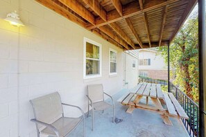 Eine überdachte Terrasse mit zwei Metallstühlen und einem Holztisch, weißen Backsteinwänden und einer Holzbalkendecke.