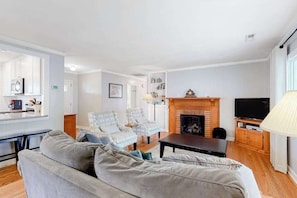 A living room with a sofa, two armchairs, a fireplace, a television, and a kitchen area with a microwave. - Oxford Lodge (Lake Junaluska)