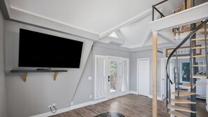 Un salon moderne doté d’un téléviseur à écran plat, d’un escalier et d’un coin repas.