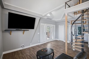 A modern living room with a flat-screen TV, a staircase, and a dining area. - Upstairs Loft on Capitol Hill Home (Seattle)