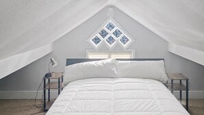 Une chambre à coucher comprenant un lit, une table de chevet, une lampe et une fenêtre ornée d’un motif en losanges.