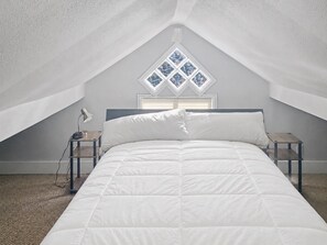 A bedroom with a bed, a nightstand, a lamp, and a window with a diamond pattern. - Upstairs Loft on Capitol Hill Home (Seattle)
