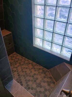 A bathroom with a hexagonal tile floor, a window with frosted glass, and a shower area. - Upstairs Loft on Capitol Hill Home (Seattle)