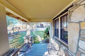 A porch with a stone wall, a swing set, and a view of a park. - Classic cottage at Burntshirt Vineyards with 2 decks - steps from tasting room (Hendersonville)