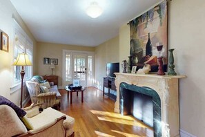 A living room with a fireplace, a sofa, a television, and a painting on the wall. - Classic cottage at Burntshirt Vineyards with 2 decks - steps from tasting room (Hendersonville)